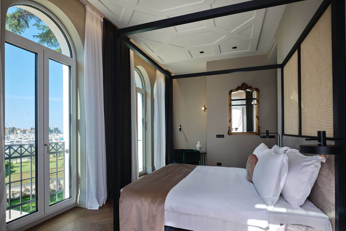 A hotel room with a large bed, a view of the marina, and a modern ceiling design.
