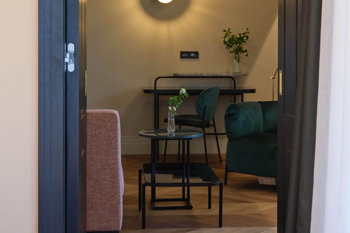 A modern living room with a sofa, a small round table, and a chair. There is a plant on the table and a wall-mounted light fixture.