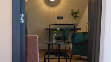 A modern living room with a sofa, a small round table, and a chair. There is a plant on the table and a wall-mounted light fixture.