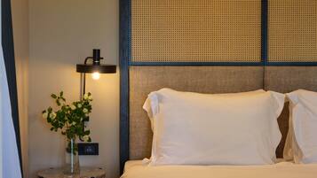 A neatly made bed with white linens, a small side table with a vase of flowers, and a wall-mounted lamp.