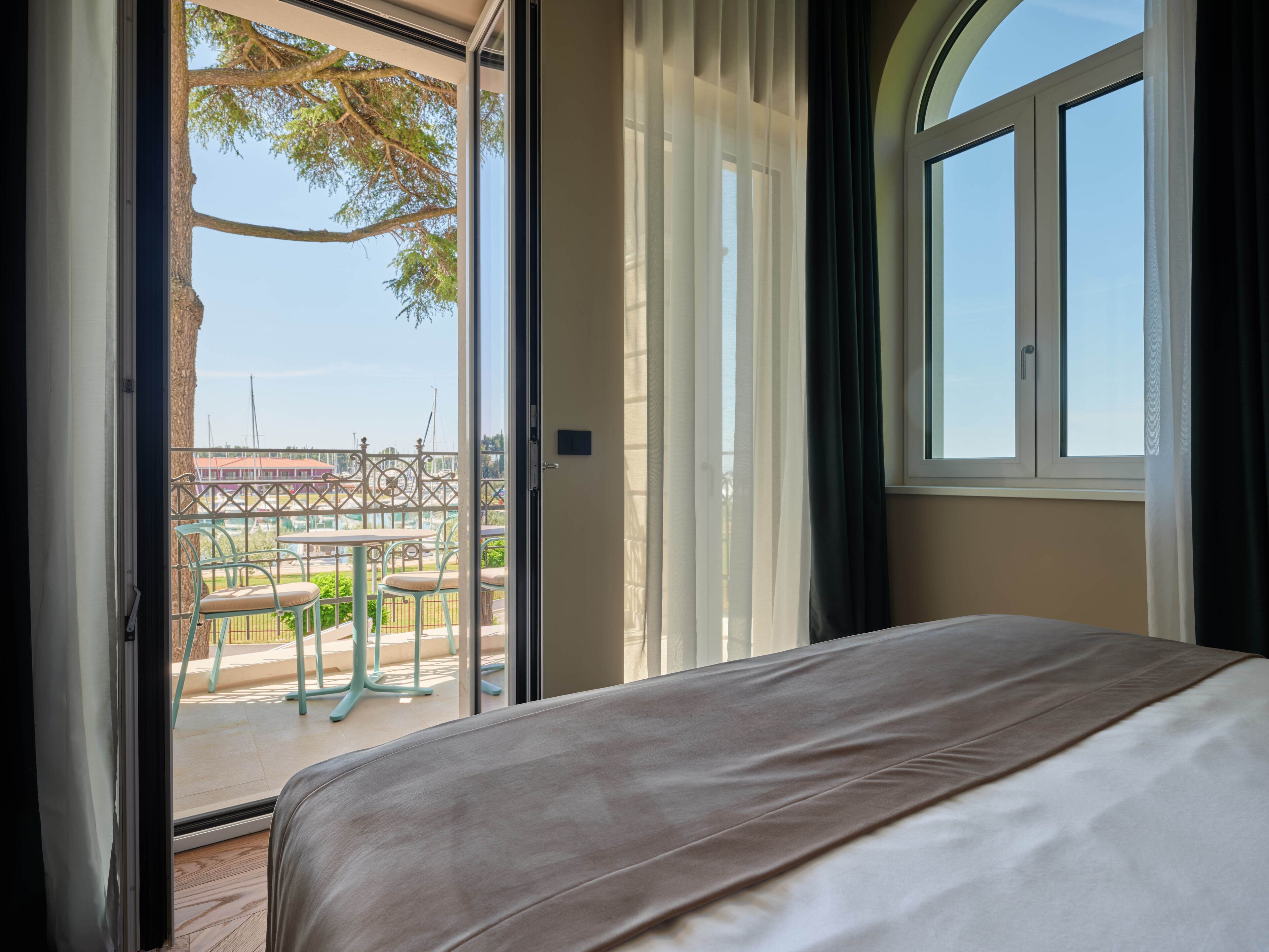 Ein Schlafzimmer mit großem Fenster und Blick auf den Außenbereich, ausgestattet mit einem Bett und einer braunen Bettdecke.