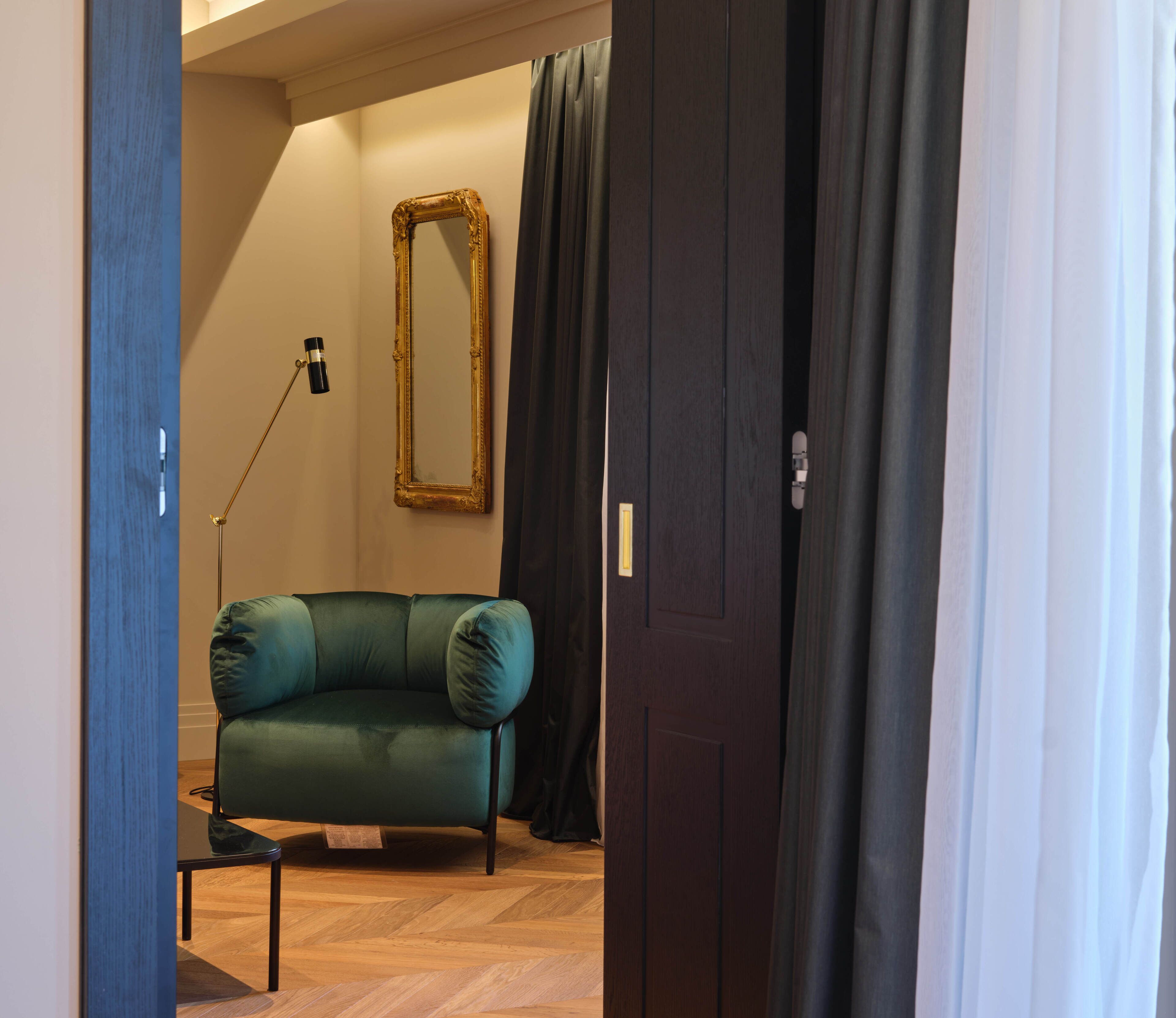 A room with a green sofa, a mirror, a floor lamp, and a door with curtains.