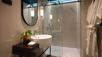 Een moderne badkamer met een douche in glazen cabine, een ronde spiegel en een witte wastafel.