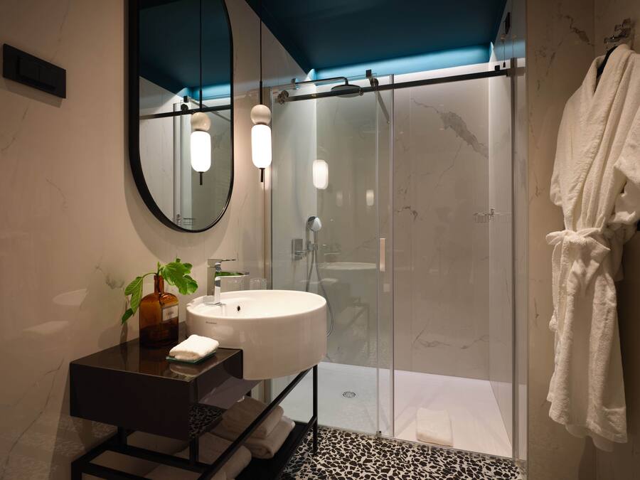A modern bathroom with a glass-enclosed shower, a round mirror, and a white sink.