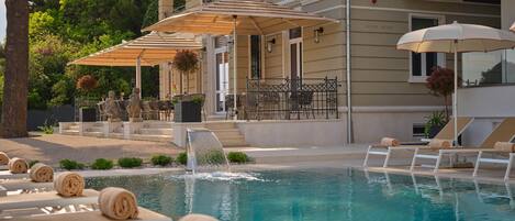 A pool area with lounge chairs and umbrellas, a statue, and a building with a balcony.