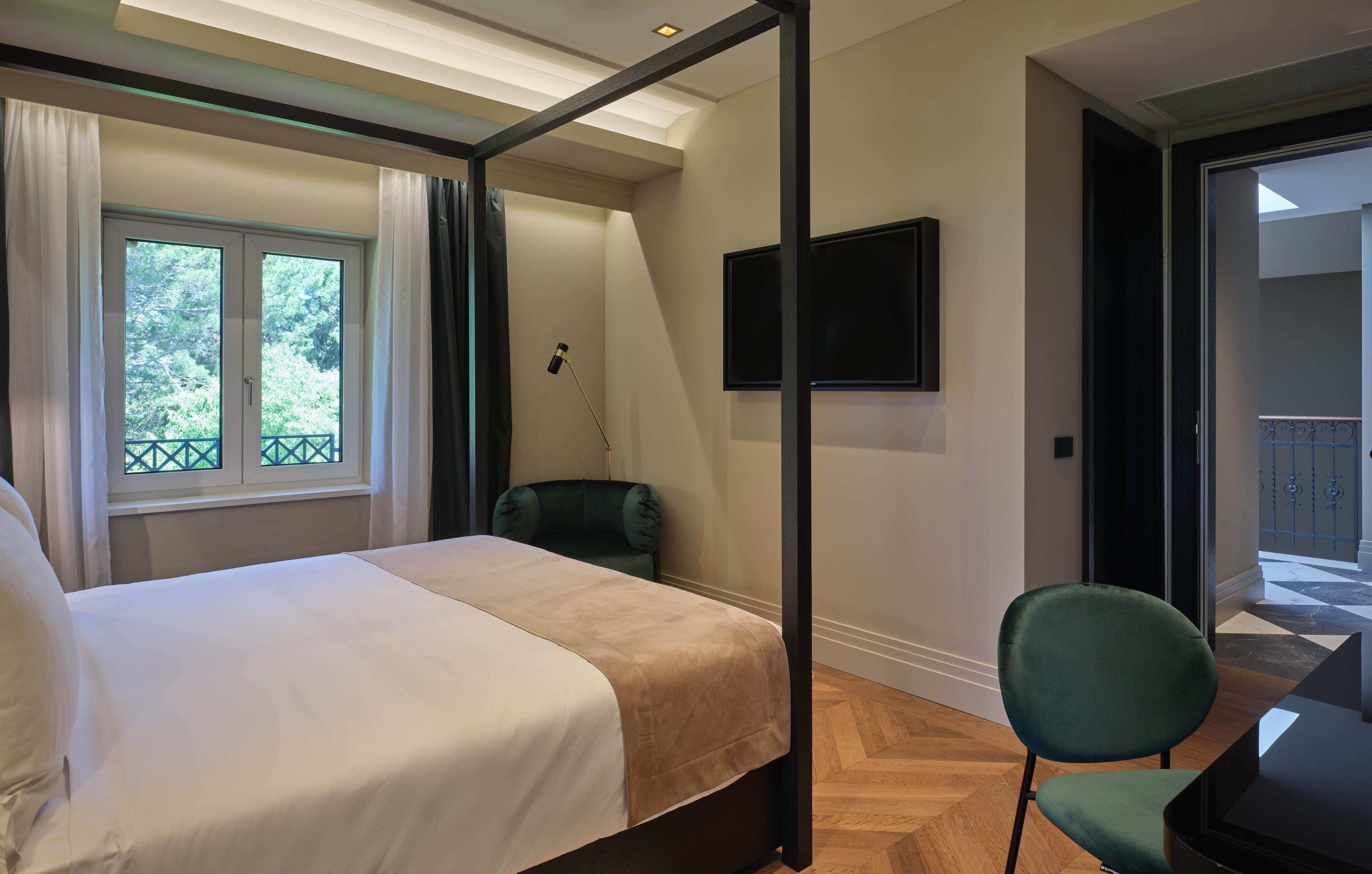 Ein Schlafzimmer mit Bett, einem grünen Sessel, einem Fernseher und Balkonblick.