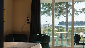 Habitació d'hotel amb un llit, dues butaques verdes, una taula i vista a un llac i arbres.