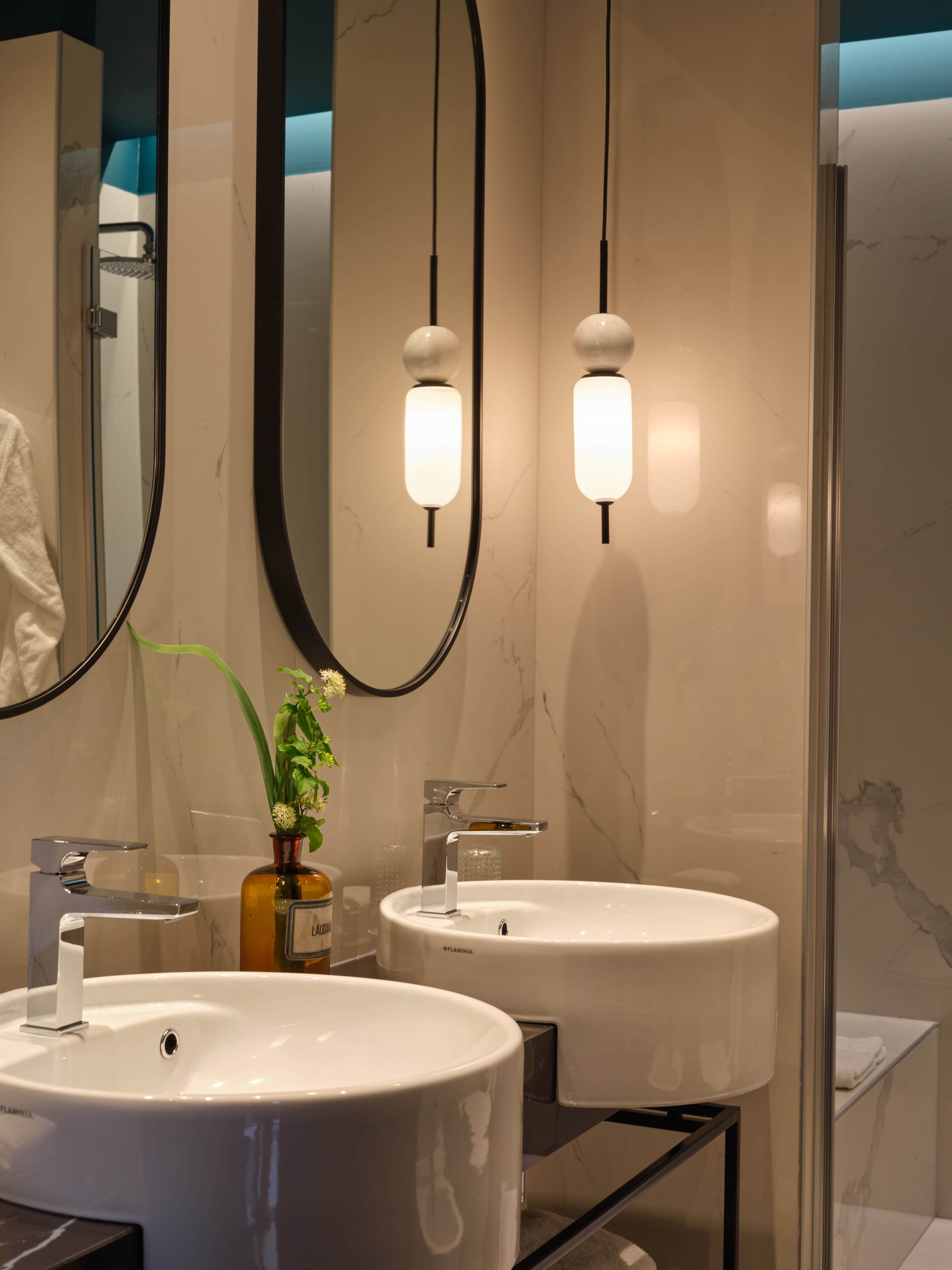 A modern bathroom with two sinks, a large mirror, and pendant lights.