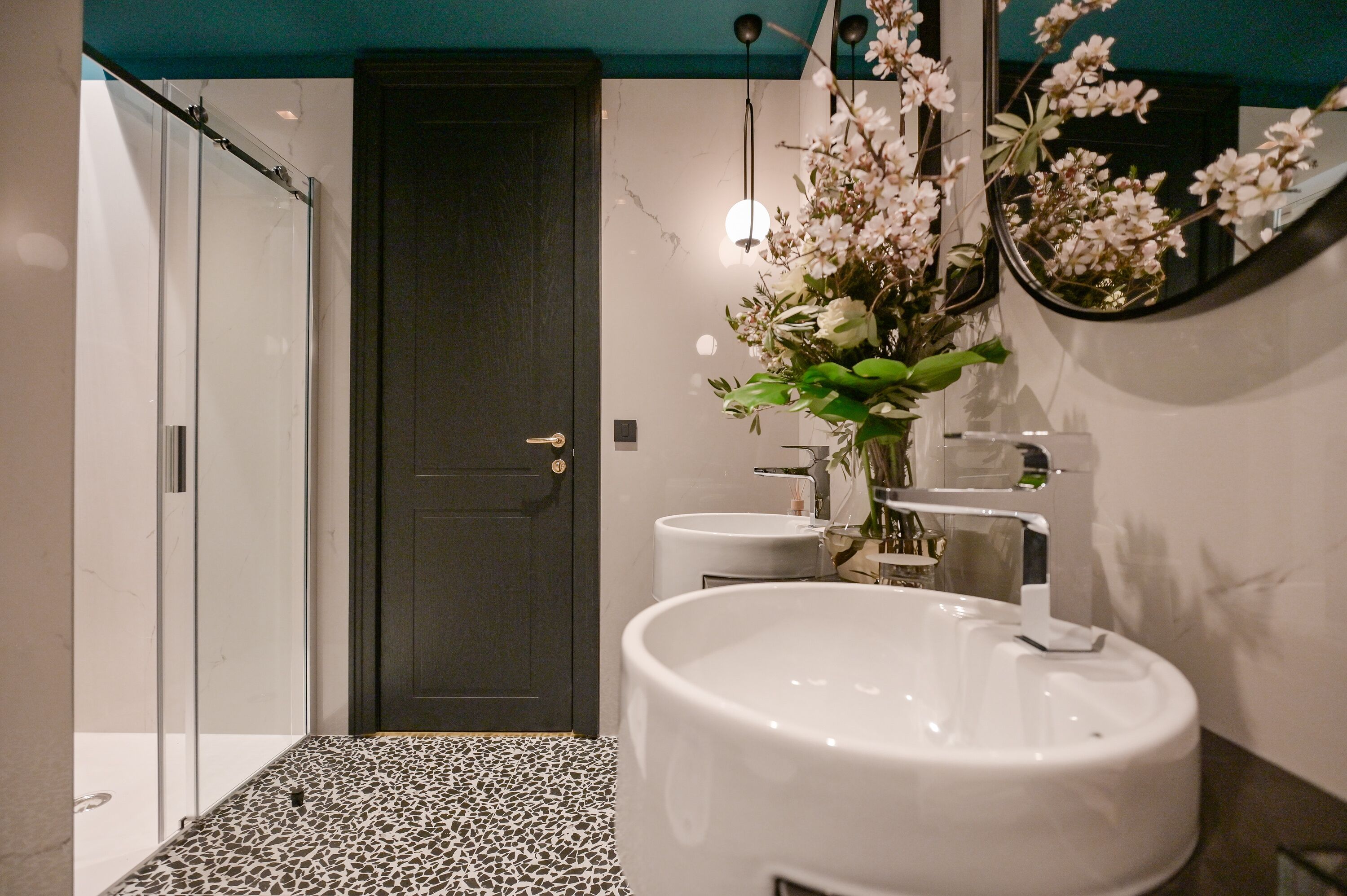 A bathroom with a large white sink, a dark door, and a mirror with flowers.