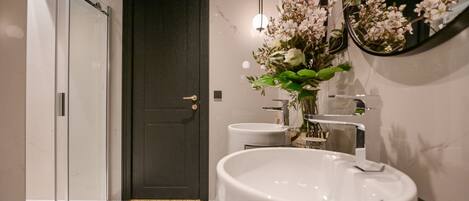A bathroom with a large white sink, a dark door, and a mirror with flowers.