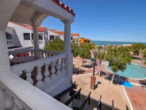 Un balcó amb barana blanca que domina una piscina i una vista despejada del mar.