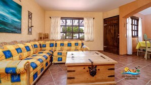 A living room with a large sofa, a wooden coffee table, and a view through the windows. - La Hacienda Condo Six (San Felípe)