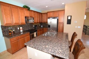 A kitchen with granite countertops, wooden cabinets, stainless steel appliances, and a dining area with chairs. - Condo 70-3 El Dorado Ranch (San Felípe)