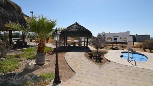 A pool area with a thatched-roof gazebo, palm trees, and a clear blue sky. - Los Sahuaros House 34 (San Felipe)