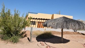 A desert-style building with a thatched umbrella, cacti, and a clear blue sky. - Los Sahuaros House 34 (San Felipe)
