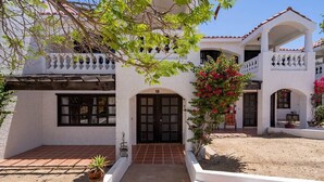 A white building with a tiled roof, a central entrance with a door, and a balcony with railings. - La Hacienda Condo 18 (San Felípe)