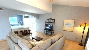 A living room with a sofa, a coffee table, a TV stand, and a kitchen area in the background. - La hacienda condo Four (San Felípe)