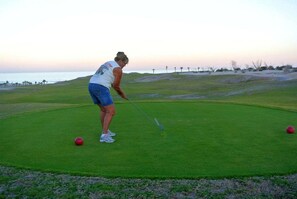 A person playing golf on a green with a view of the ocean in the background.