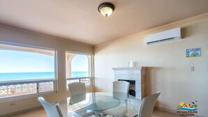A dining area with a glass table and chairs, a fireplace, an air conditioning unit, and a view of the sea.