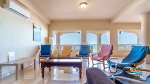 A spacious room with a pool table, multiple lounge chairs, and large windows offering a view of the sea.