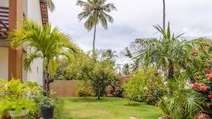 A well-maintained garden with various plants and a palm tree. - IT16 Apt 2 Quartos a 150m da Praia (Camaçari)
