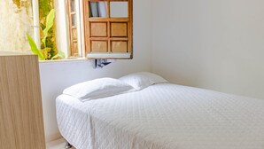 A bedroom with a single bed, a wooden headboard, a window with a wooden frame, and a view of a plant outside. - IT16 Apt 2 Quartos a 150m da Praia (Camaçari)