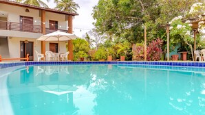 A swimming pool with a blue tiled edge, surrounded by potted plants and outdoor furniture. - IT16 Apt 2 Quartos a 150m da Praia (Camaçari)