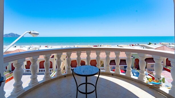 Ein Balkon mit Tisch und Stühlen mit Blick auf einen Strand und das Meer.