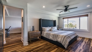 A bedroom with a large bed, a nightstand, a ceiling fan, and a window with a view. - Ocean views includes Golf Cart - 611 Newhaven (Fripp Island)