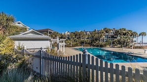 A pool area with a white fence, palm trees, and a building with a sloped roof. - Ocean views includes Golf Cart - 611 Newhaven (Fripp Island)