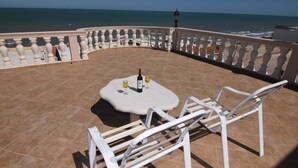 Eine Terrasse mit Tisch und Stühlen, einer Weinflasche und Blick aufs Meer.