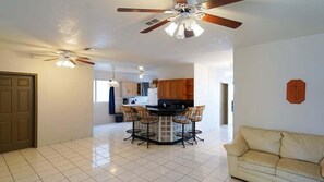 A spacious living area with a kitchen, dining area, and a ceiling fan.