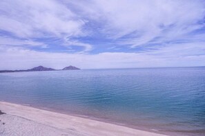 A beach with clear water and distant mountains.