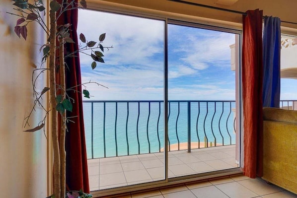 A room with a large sliding glass door leading to a balcony with a view of the sea.
