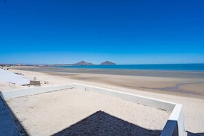 Uma praia com céu claro, faixa de areia e montanhas ao longe.