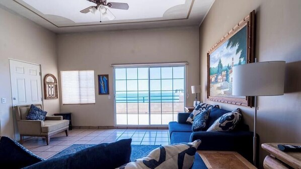 A living room with a large window, a ceiling fan, a sofa, and a painting on the wall.