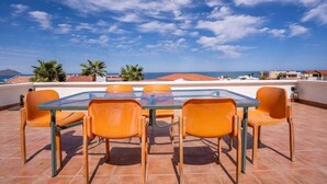 A glass-top table with four orange chairs on a tiled patio with a view of the sea and mountains. - Rick`s Private POOL House (San Felípe)