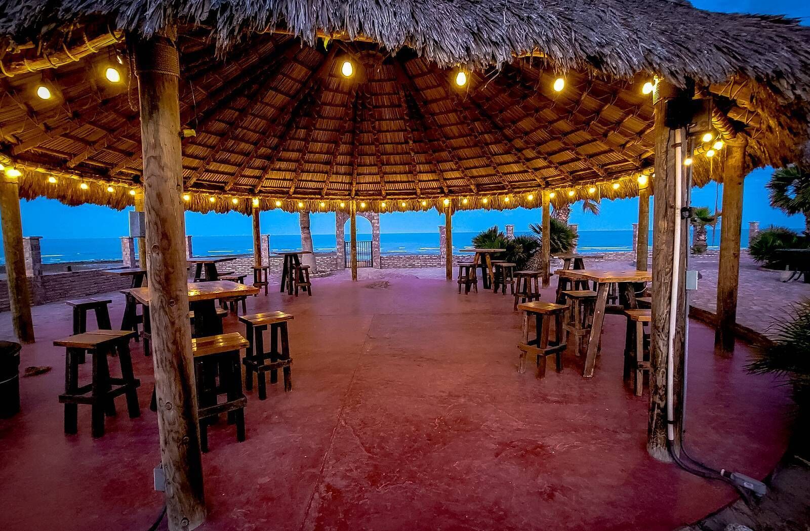 Un espace de restauration en plein air doté de toits de chaume et illuminé de guirlandes lumineuses, avec vue sur la plage.