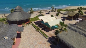 Un resort con cabañas de techo de paja, una piscina y vista a la playa.