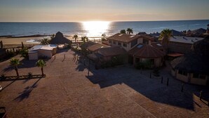 Un patio frente a la playa con edificios, palmeras y vistas al océano al atardecer.