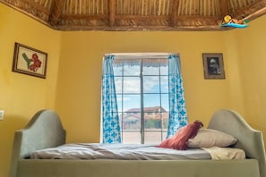 A room with a bed, a window with blue patterned curtains, and a thatched roof. - 1-Bedroom Beach Studio  - Serene getaways. (San Felipe)