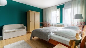 A bedroom with a bed, a wooden wardrobe, a sofa, and a window with curtains. - Familienfreundlich - Farbenfroh - Außergewöhnlich (Braunlage)