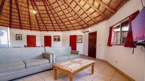 A room with a thatched roof, a sofa, a wooden table, and a TV.