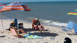 Une plage avec des parasols à rayures, des chaises de plage et une personne assise sur une chaise.