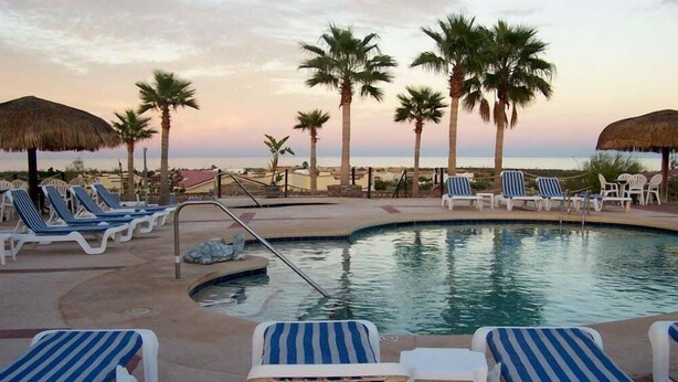 Un espace aménagé au bord de la piscine, avec des chaises longues, des palmiers et une vue imprenable sur le coucher de soleil.