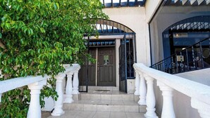 Une entrée d’immeuble avec une porte grillagée, une balustrade blanche et des marches menant à l’entrée.