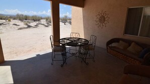 An outdoor patio with a round table and chairs, a sofa, and a decorative wall piece.