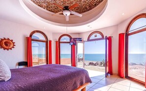 Ein Schlafzimmer mit einem großen Bett, einem Deckenventilator und Blick auf den Strand durch große Fenster.