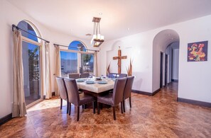 Uma sala de jantar com uma mesa de mármore, cadeiras, um candelabro e uma cruz na parede.