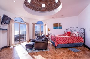 Quarto com cama, sofá, televisão e vista para o mar.